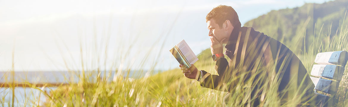 man reading a book on a coastal bench