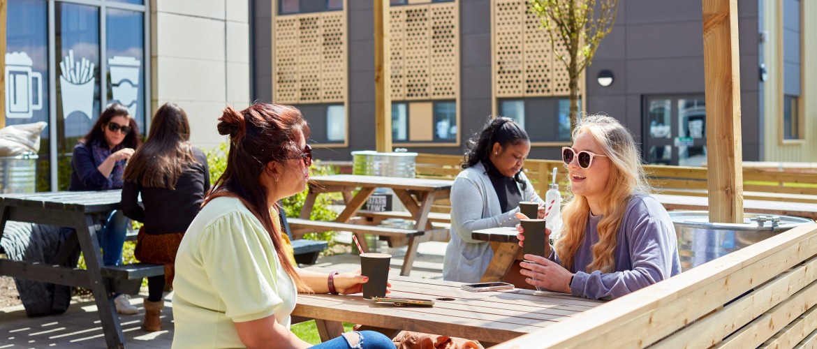 two female students sat on a bench outside Tafarn Tawe 