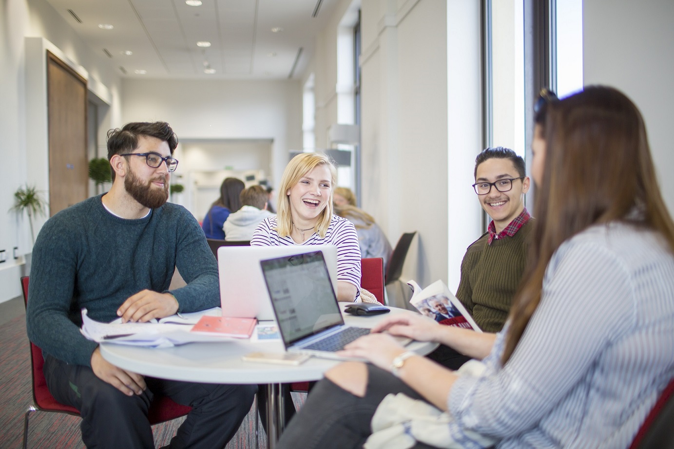 University students sitting around a desk and smiling 