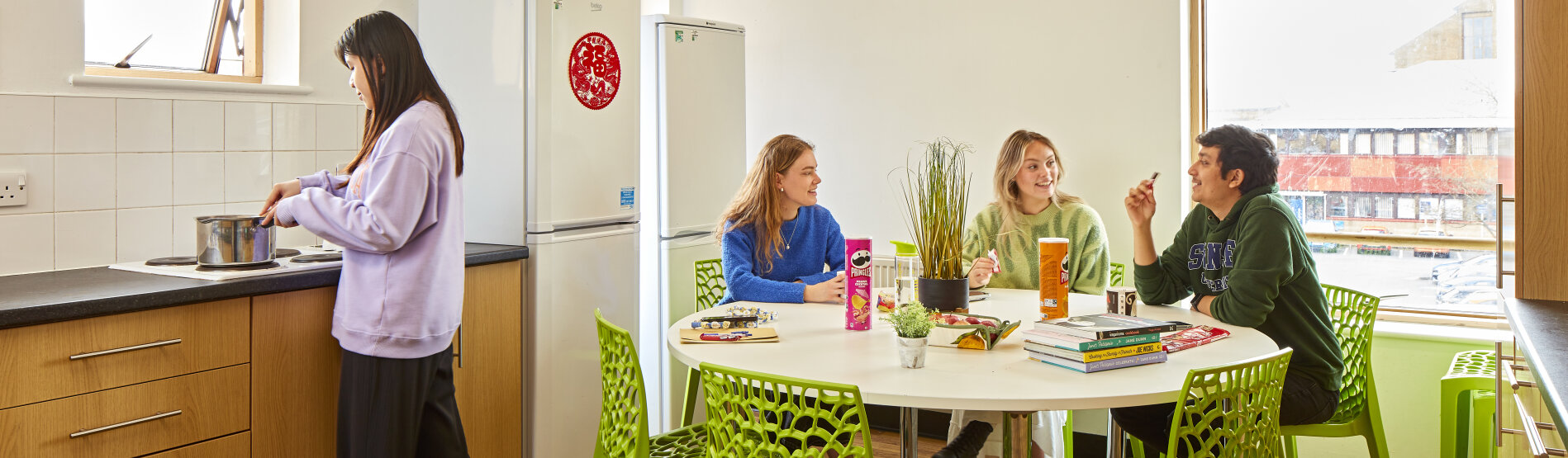 students sitting around a kitchen table in halls of residence, chatting happily