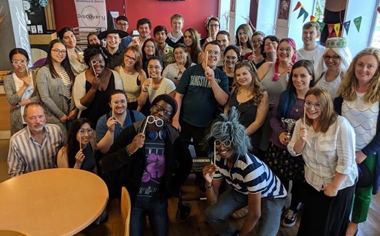 A large group of Discovery volunteers posing with party props, such as glasses on sticks.