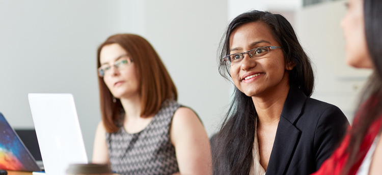 Three women around a table listening to someone speak