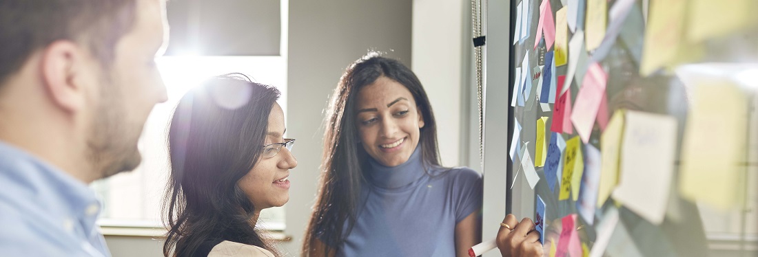 Image of students brainstorming infront of a whiteboard with sticky notes on. 