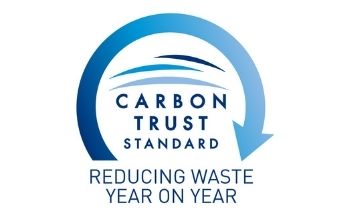 Logo Safon Gwastraff yr Ymddiriedolaeth Garbon. Hanner cylch wedi ei adeiladu o saeth las gyda'r geiriau Carbon Trust Standard y tu mewn a'r geiriau Lleihau Gwastraff Flwyddyn ar Flwyddyn isod. Yn erbyn cefndir gwyn.