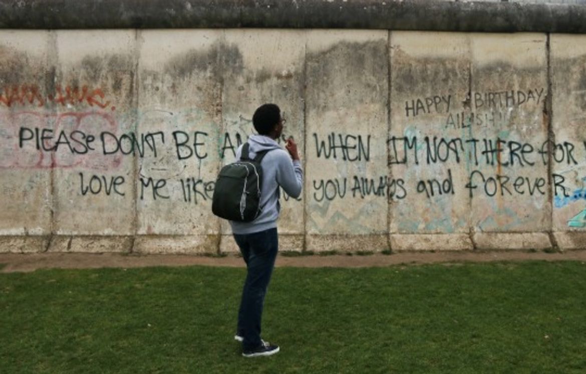 twrist yn edrych ar wal berlin, sydd gyda graffiti arno