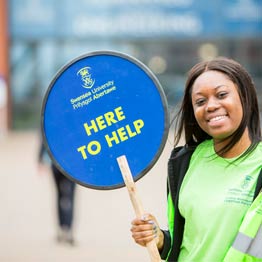 llysgennad myfyriwr yn dal arwydd 'here to help'