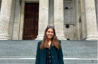 Student standing outside building with steps and large pillar