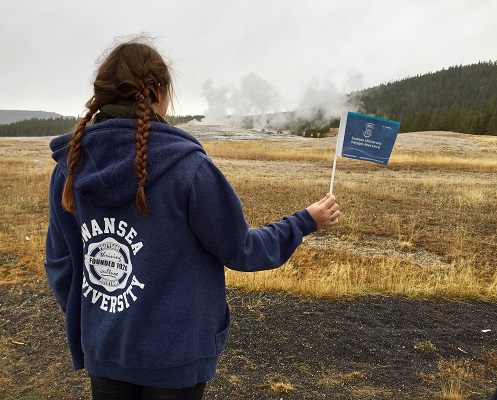 Myfyrwraig yn dal baner Prifysgol Abertawe yn yr awyr agored yn wyoming