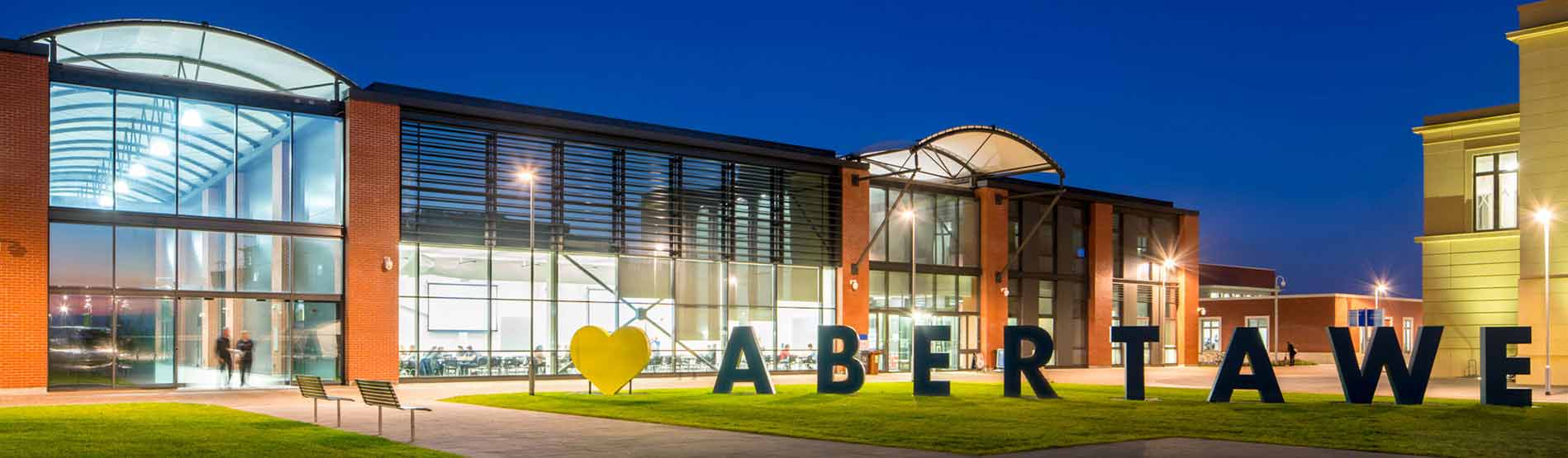 Abertawe sign lit up at night on the green outside Engineering Central Building at Swansea University's Bay Campus