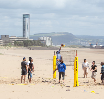 Myfyrwyr ar y traeth yn chwarae pêl foli. 