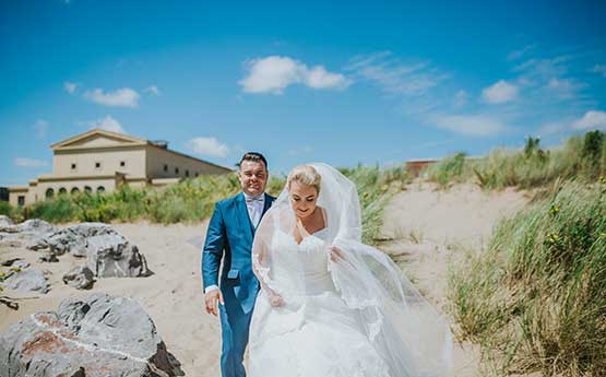 Couple have their wedding photos taken on beach in front of Great Hall