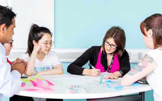 a group of people sat around a table, the table has flipchart and post it notes