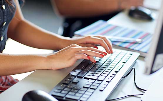 Image of hands wearing red nail polish typing on a black computer keyboard