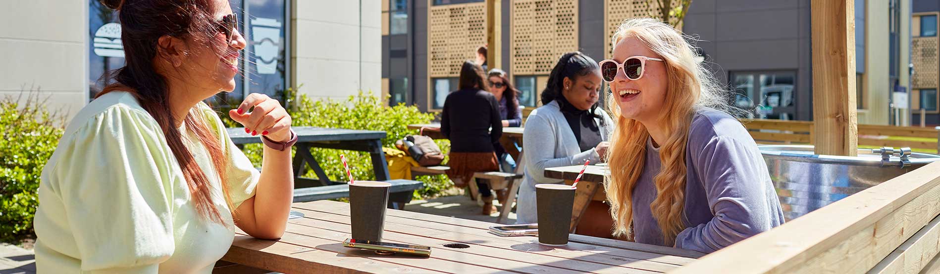 Two students sitting outside Tafarn Tawe at the Bay Campus drinking coffee and chatting.