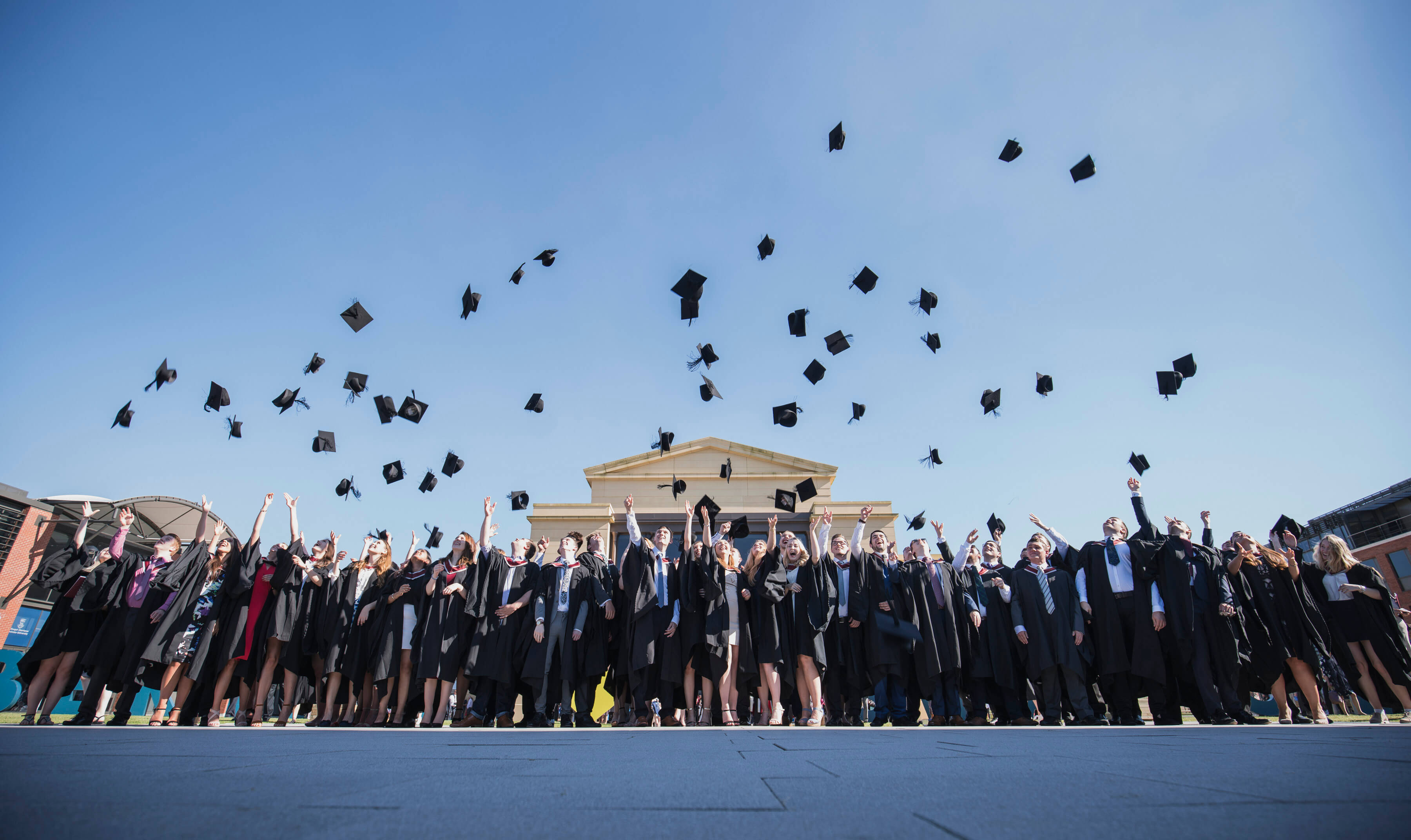 A large group of graduates in front of the Great Hall throwing mortarboards