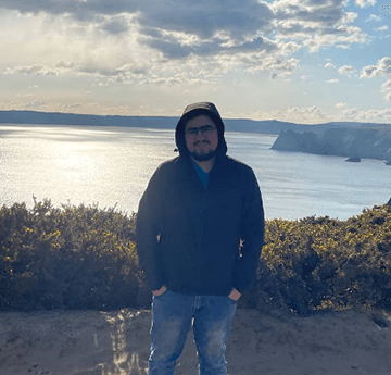 A photo of User, one of our students standing in the sand dunes on the background of sea a cliffs on a sunny day.