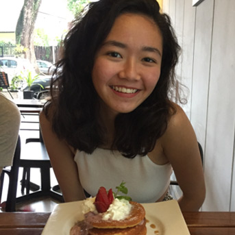 Malaysian student smiling at the camera sitting at the table eating a meal