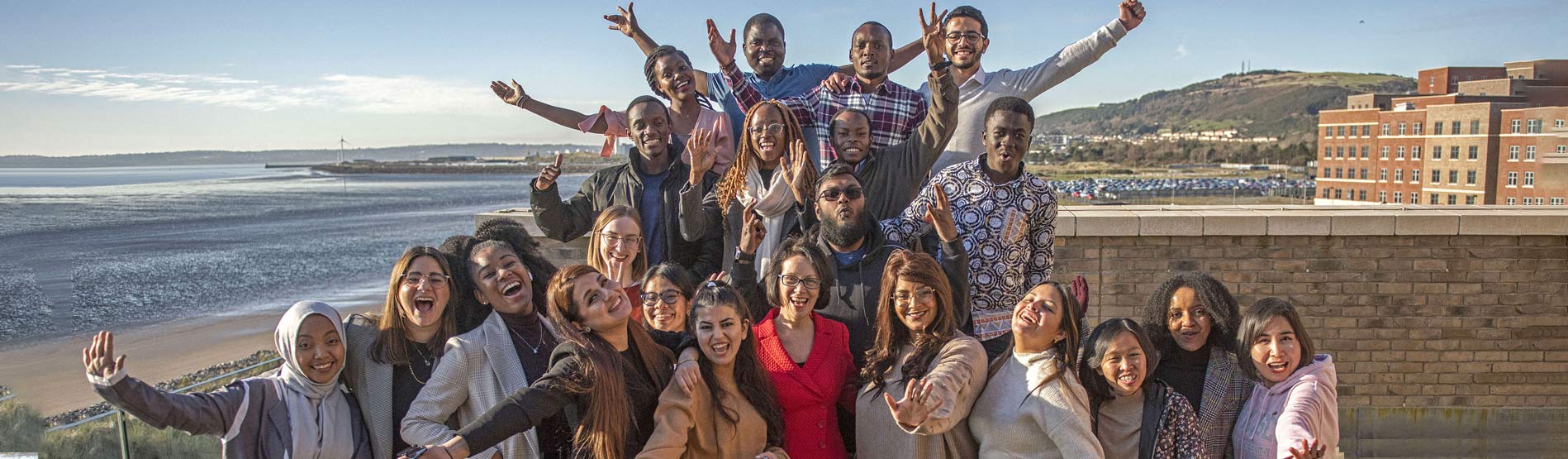 A photo of a large group of Swansea university Chevening Scholars during their casual meet up with Swansea Bay in the background.