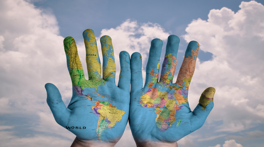 World map painted across two hands. Blue sky in the background.