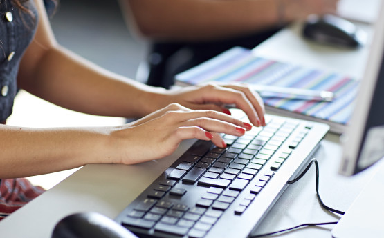 Hands with nails painted red are typing at a keyboard.