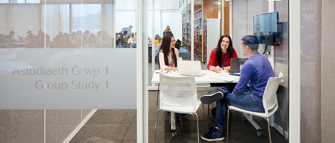 Students sitting on white chairs around a white table in a glass fronted study pod.