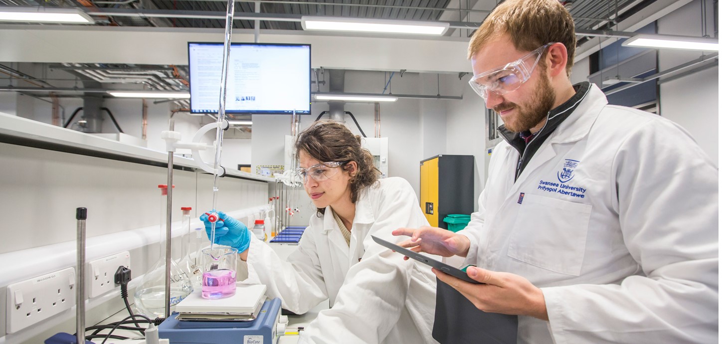 man and woman scientist in lab wearing white lab coats and clear goggles