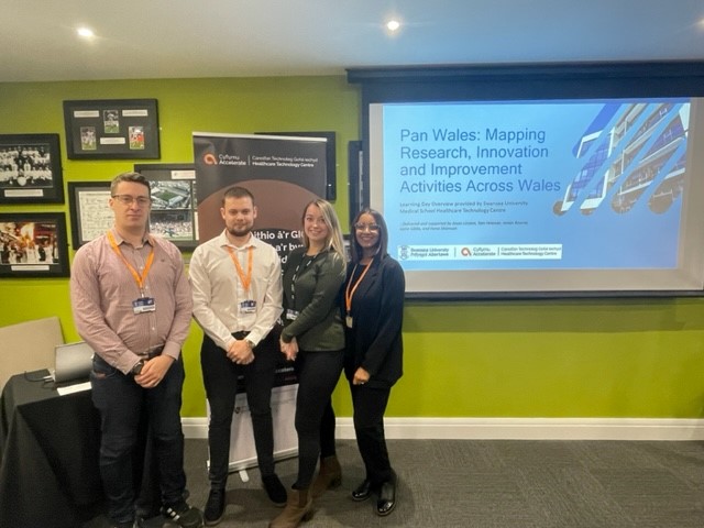 HTC team standing in front of presentation screen in Swansea.com Stadium with 'pan-wales learning day' slide