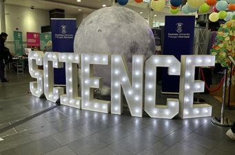 science letters in lights in front of moon sculpture