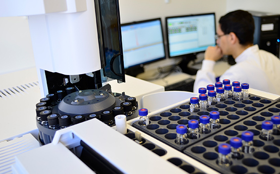 Samples in a machine with researcher on computer in the background