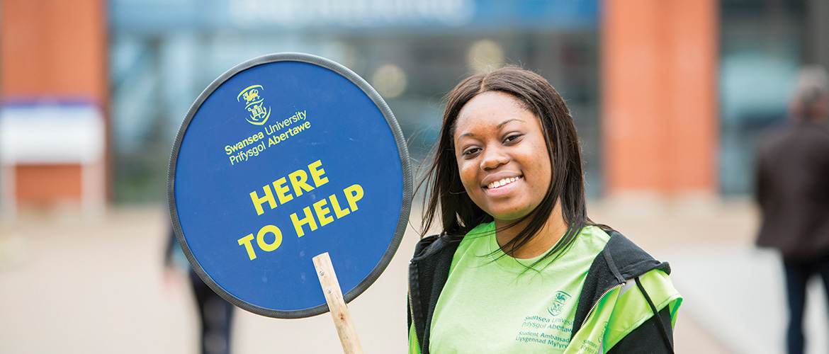 Female student ambassador holding a here to help sign.