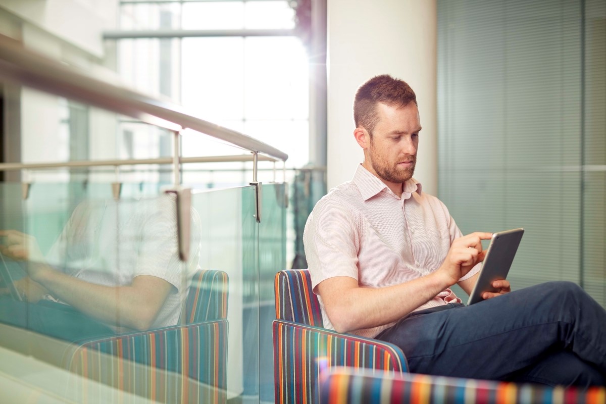 Man seated on a stripy chair and looking at an iPad