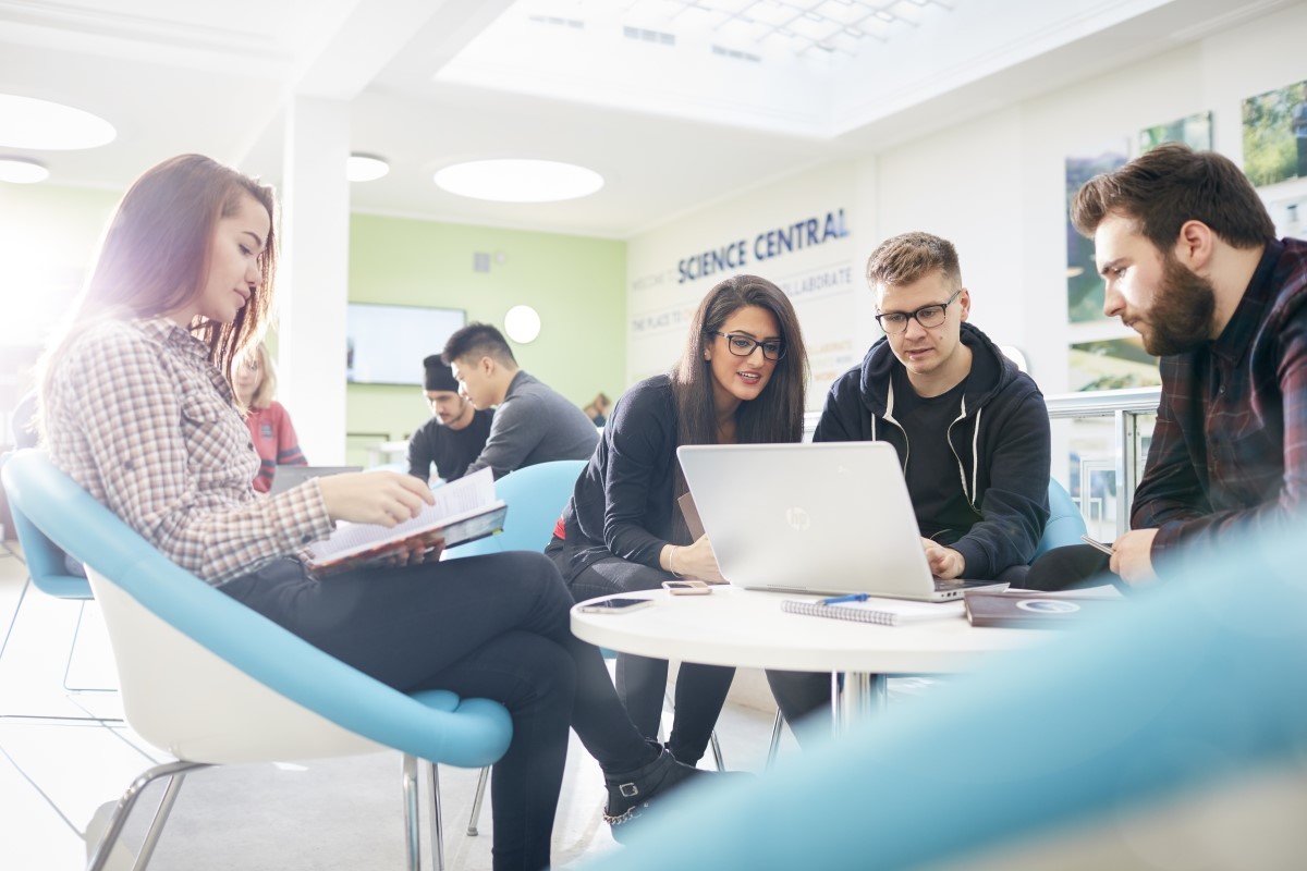 Group of students chatting and looking at a laptop computer.