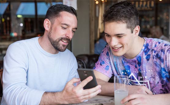 Two male students looking at something on a mobile phone sat at a table