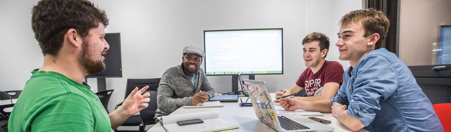 Postgraduate students doing collaborative work at a table with a lit but blank screen