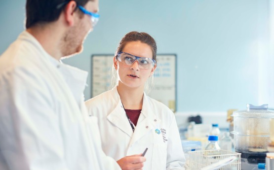 Man and woman wearing lab coats standing in a lab.