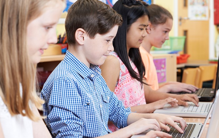 A row of primary school children sitting at computers in a classroom setting