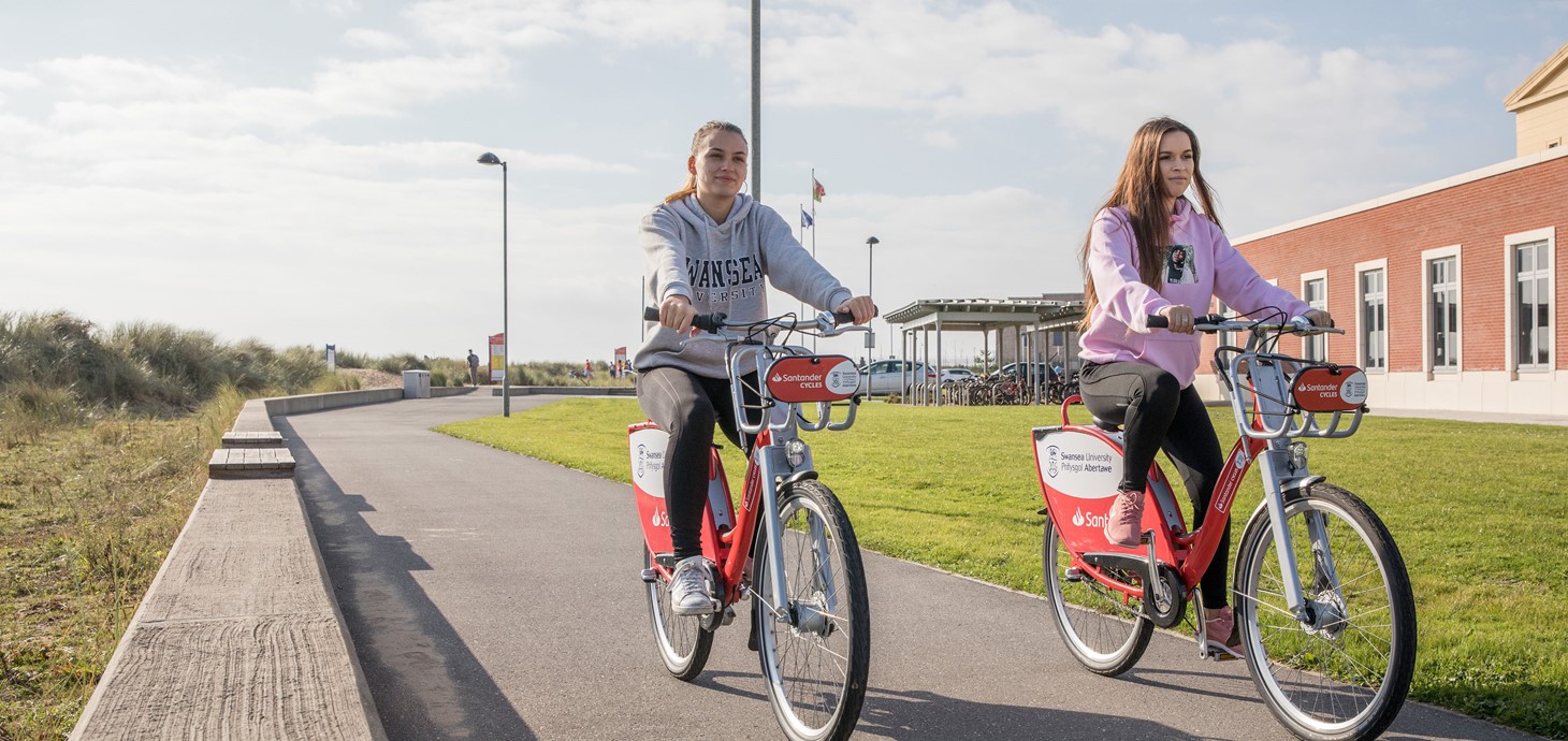 Two students ride on Santander cycles at the Bay Campus. 