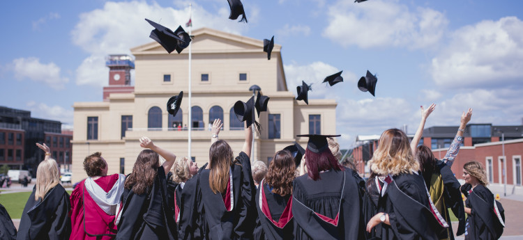 Students celebrate their graduation by throwing mortarboards in the air.