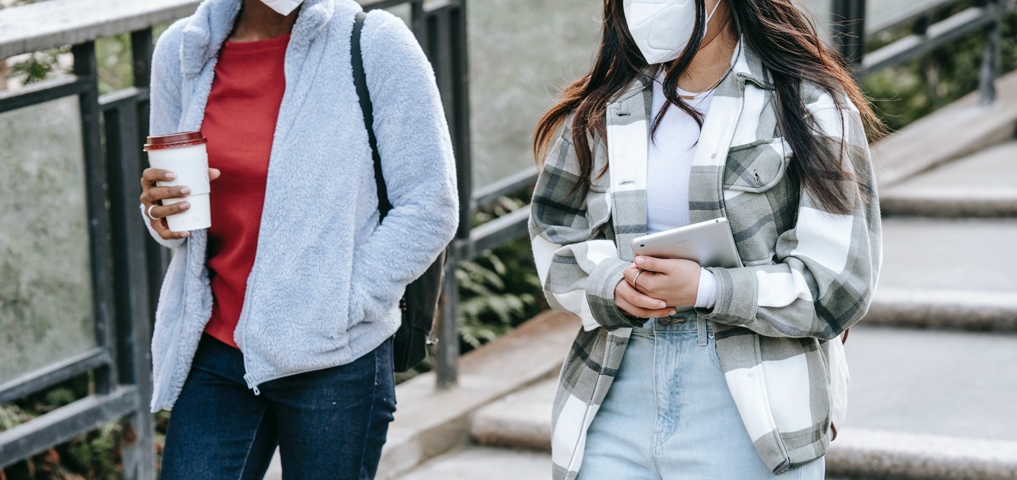 Two teenagers pictured from shoulders down walking side by side down steps, one holding a coffee, one holding a tablet