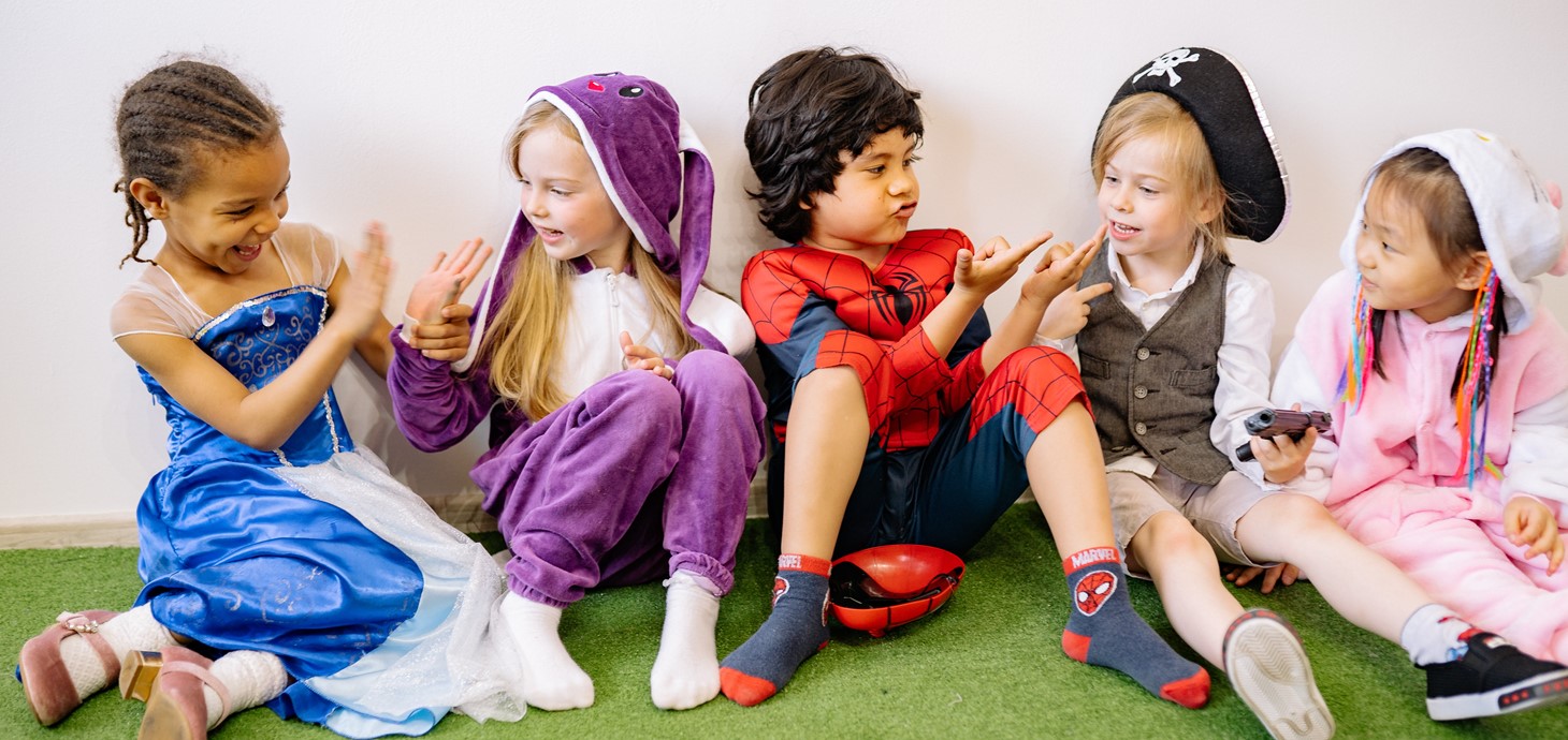 Group of five young children, wearing fancy dress sitting on a carpet playing and laughing together