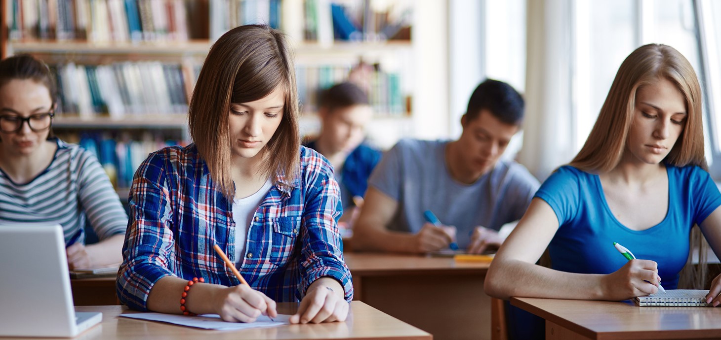 A photo of students sitting at desks and writing.