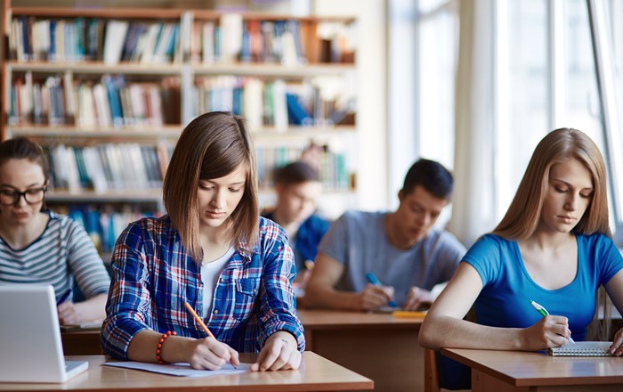 A photo of students sitting at desks and writing.