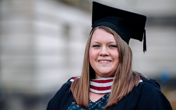 A photo of Bethany Kelly on her graduation day. Bethany is wearing her cap and gown.