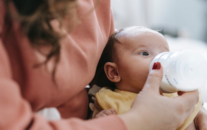 Mother feeding infant with milk from a bottle.