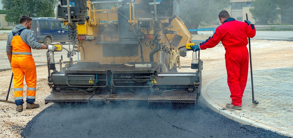 Two men spreading tarmac onto road.