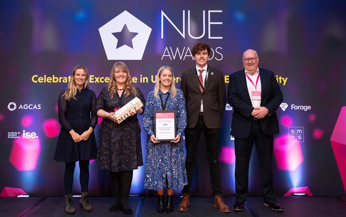 Three women and two men standing in a row at an awards ceremony.