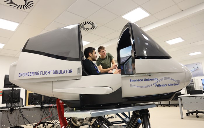 Man sitting in a flight simulator while another looks in