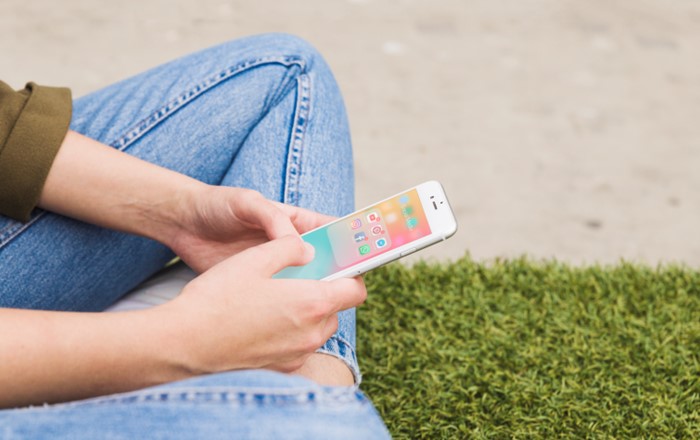 A person sits on the floor as they search for social media apps on their phone.