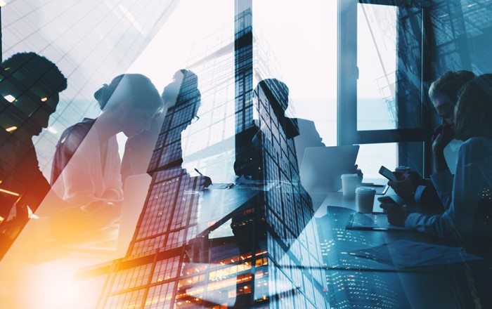 Silhouette of people sitting meeting table with image of high-rise building superimposed on top