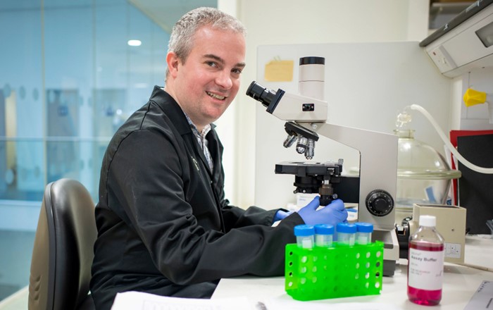 Male scientist in laboratory sat by microscope